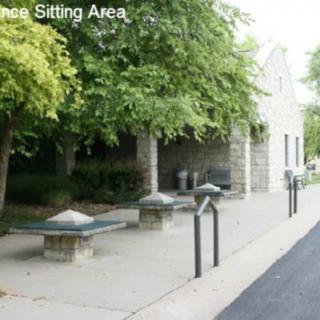 An outdoor sitting area with benches surrounded by trees and a stone building.