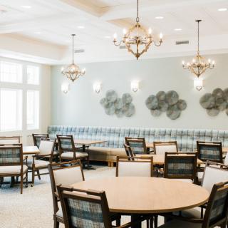 A well-lit dining area with round tables, chairs, chandeliers, and decorative wall art.