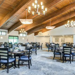 A spacious and elegantly designed dining area with multiple tables and chairs, featuring a wooden ceiling and chandeliers.