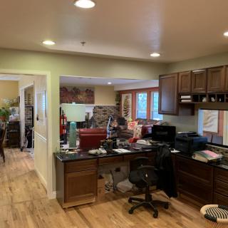 A cozy home office setup in a spacious open plan area, featuring a desk and chair, computer, and kitchen cabinets.