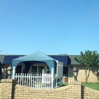 A house with a blue canopy set up in the yard, surrounded by a brick fence on a sunny day.