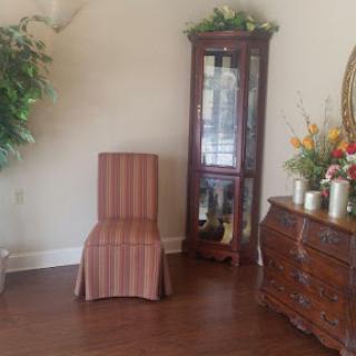 A cozy corner of a room featuring a striped chair, an elegant display cabinet, and decorative flowers.