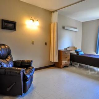 A minimalist room featuring a bed, recliner, and wooden dresser.