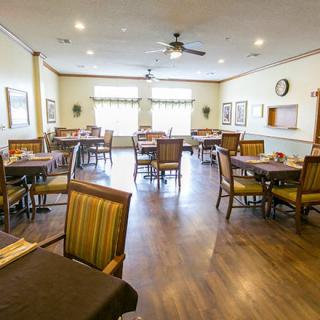 A spacious dining room with multiple tables and chairs, featuring wooden floors and large windows.