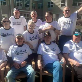 A group of elderly people wearing matching t-shirts posing together outdoors on a sunny day.