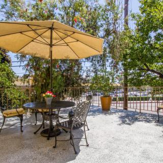 A sunny outdoor patio with a table, chairs, and a large umbrella surrounded by trees.