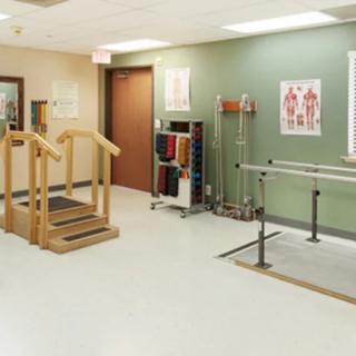 A rehabilitation room equipped with physical therapy equipment including parallel bars and a staircase.