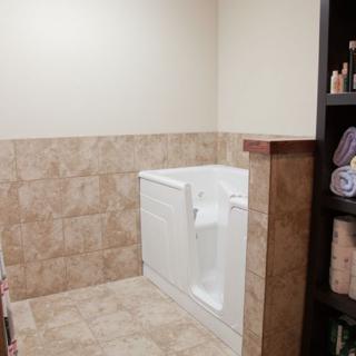 A well-designed bathroom featuring a walk-in tub and tiled walls, with a shelf stocked with towels and toiletries.