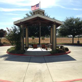 A charming outdoor pavilion with seating, surrounded by greenery and featuring the American flag.