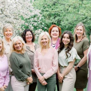 A group of women posing together outdoors in front of trees.