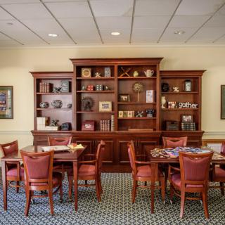 A well-furnished library room featuring wooden bookshelves, tables, and chairs.