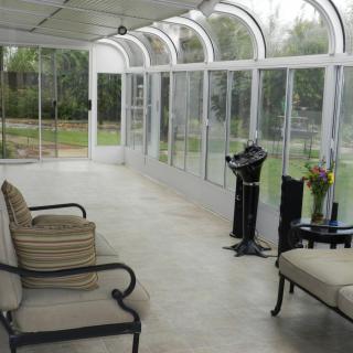 A bright sunroom with glass walls offering a garden view, featuring comfortable seating and elegant decor.