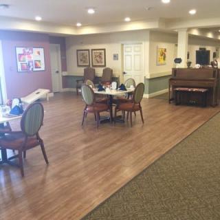 A well-lit dining area with tables, chairs, and a piano along with decorative artwork on the walls.