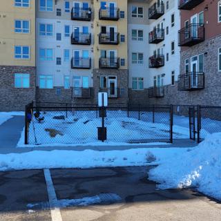 A snowy parking lot in front of an apartment building, showcasing a blend of urban living and winter weather.