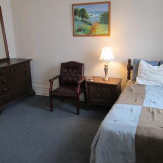 A cozy bedroom with a bed, dresser, chair, and a lamp on the nightstand.