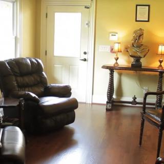 A cozy living room with armchairs, a wooden floor, and decorative elements such as lamps and a bust sculpture.