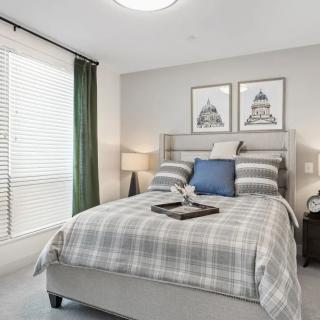 A cozy, modern bedroom with plaid bedding, artwork above the bed, and a tray on the bed.