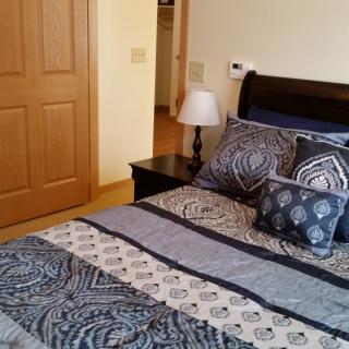 A cozy bedroom with a neatly made bed featuring patterned pillows and a bedside lamp.