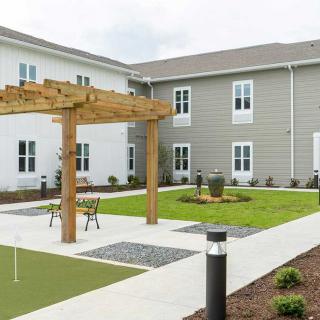 A modern courtyard with outdoor seating, a wooden pergola, and landscaped green space.