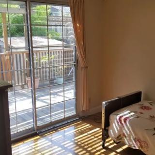 A cozy bedroom with sunlight streaming through a sliding glass door, leading to a balcony.