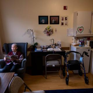 An elderly person reading in a comfortable living room setting with a walker nearby.