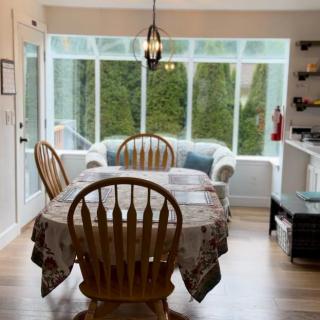 A cozy dining area with a wooden table and chairs, abundant natural light from large windows, and a comfortable sofa.