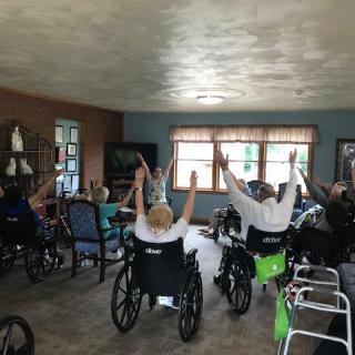 A group of elderly individuals participating in an indoor exercise session while seated in wheelchairs.