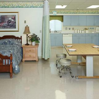 A room with a bed and a kitchen area, featuring wooden furniture and a dining table.