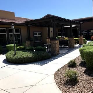 A view of a well-maintained building entrance with landscaped gardens and a shaded area.