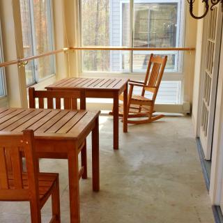 A sunlit room featuring wooden tables and chairs, including a cozy rocking chair.