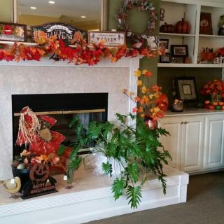 A cozy fireplace adorned with vibrant fall decorations, including leaves and pumpkins, creating a warm autumn atmosphere.