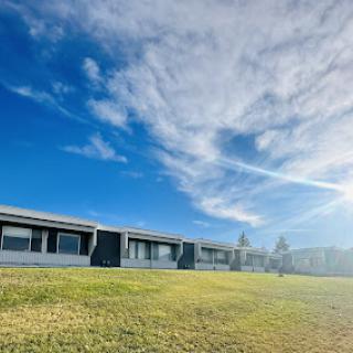 A serene view of a building under a bright blue sky with soft clouds and sunlight illuminating the grassy area.