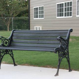 A black metal bench situated on a paved area near a building with windows.