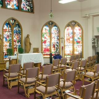 An empty chapel with stained glass windows and arranged seating facing an altar.