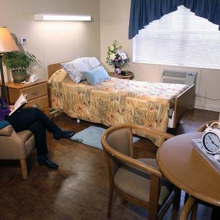 A hospital room with a bed, table, chair, and a person sitting.