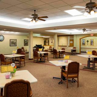 A spacious community dining area featuring tables and chairs, illuminated by ceiling fans and soft lighting.