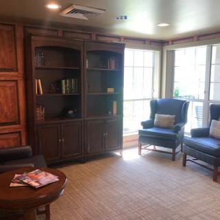 A cozy living room with a bookshelf, two armchairs, and a coffee table near large windows.