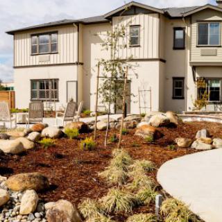A modern home with a landscaped front yard featuring rocks and diverse plants.