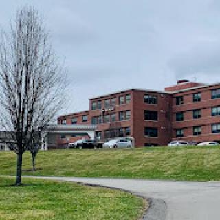 A view of a medical facility set against a cloudy sky, surrounded by grass and a leafless tree.