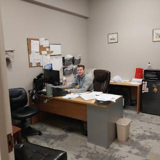 An office space featuring a desk, computer, and an individual working amidst documents.
