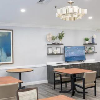 A modern dining area with tables and chairs, decorated with a painting, shelves, and a TV.