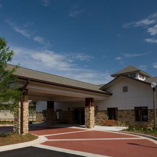 A modern building with a covered entrance and landscaped surroundings under a clear blue sky.