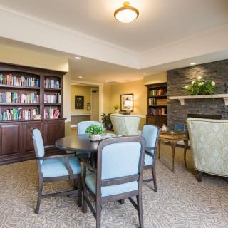 A cozy reading room featuring a bookshelf, table, and chairs under warm lighting.