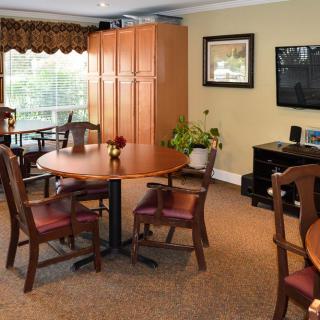 A cozy living room with a wooden table, chairs, and a flat-screen TV on the wall.