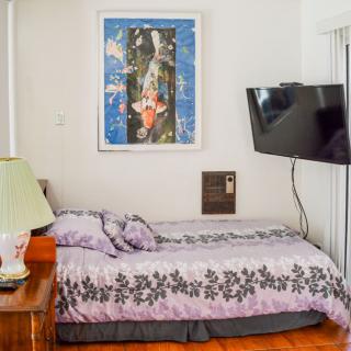 A cozy bedroom with a bed, wall art, and mounted television.