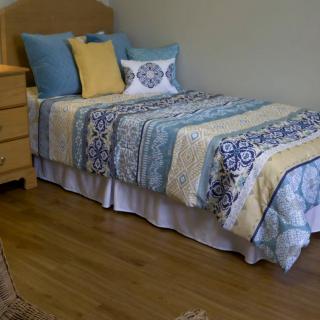 A neatly made bed with patterned bedding and pillows in a room with wooden flooring.