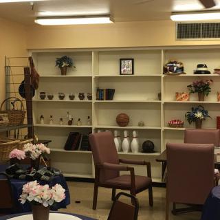 A room with shelves displaying various decorations, surrounded by tables and chairs.