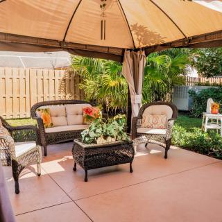 A cozy outdoor patio under a gazebo, featuring comfortable wicker furniture and lush garden surroundings.