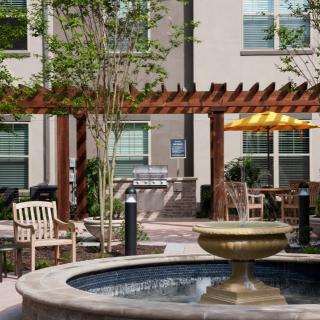 A peaceful courtyard with a central fountain, surrounded by outdoor seating and a wooden pergola.