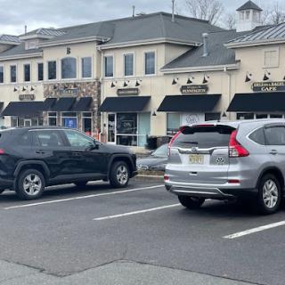 A view of a parking lot in front of retail storefronts, featuring two parked cars.